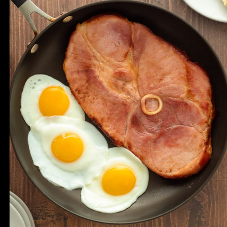 a slice of bone in ham fried in a pan with eggs