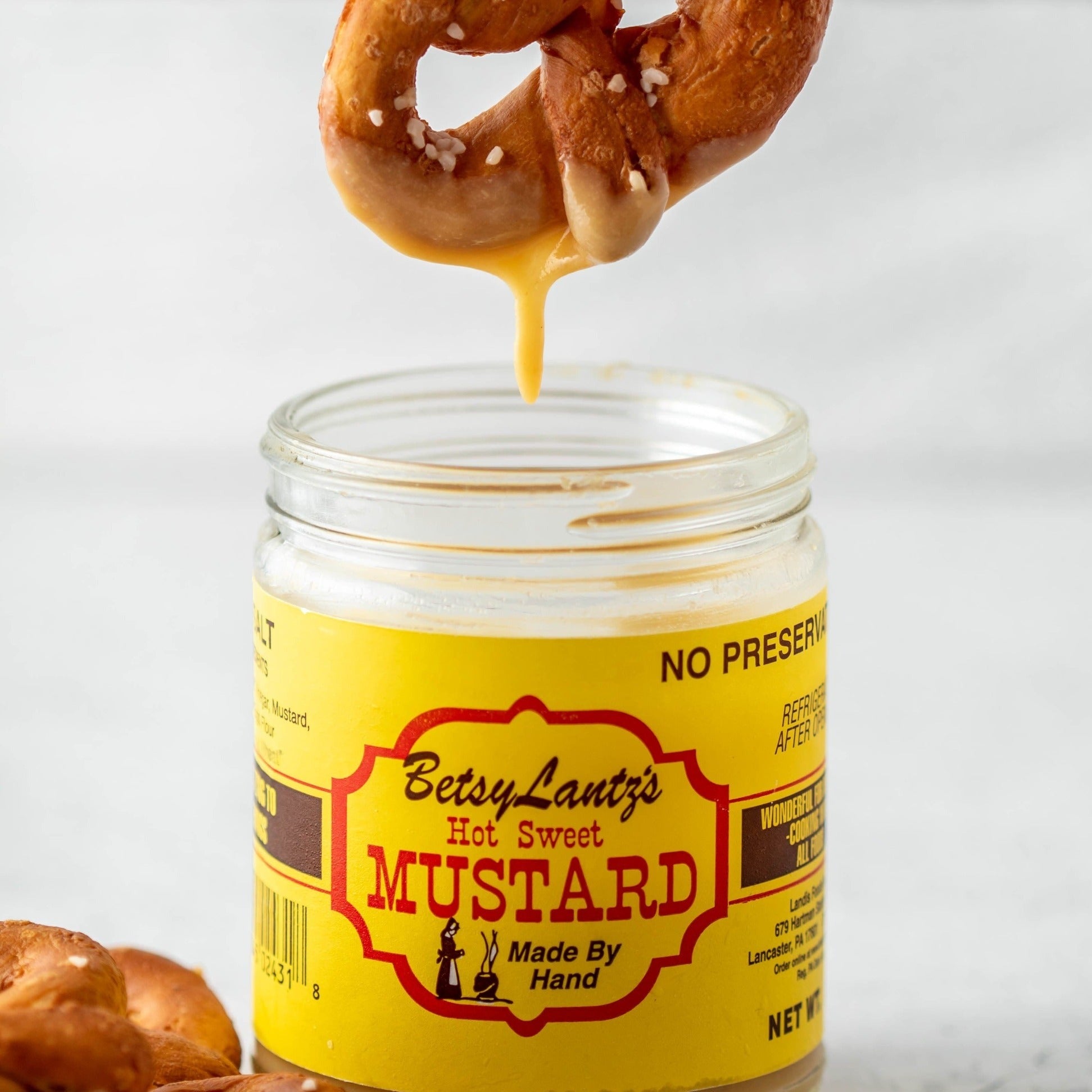 a pretzel being dipped into a jar of mustard