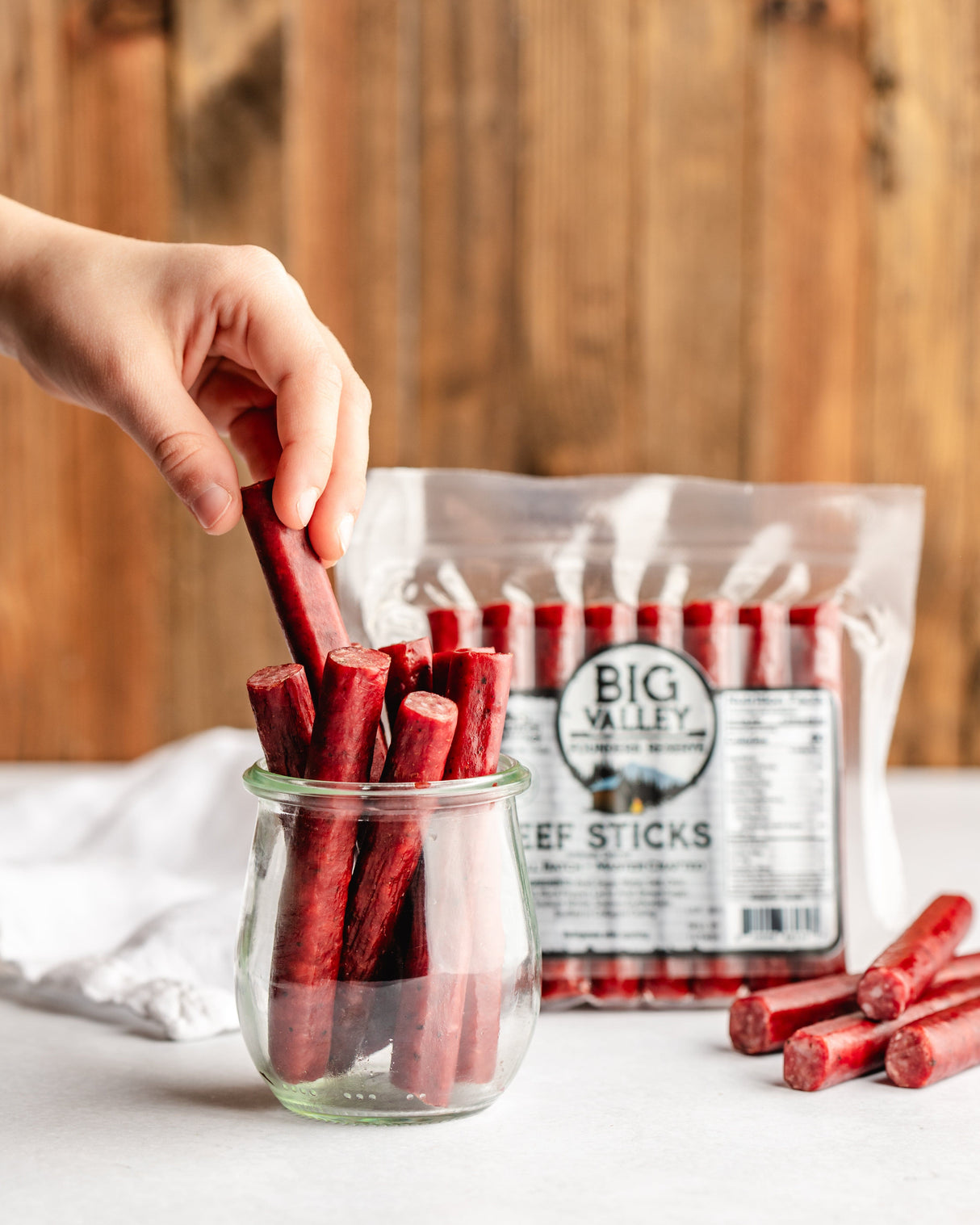 a hand grabbing a beef snack stick from a jar