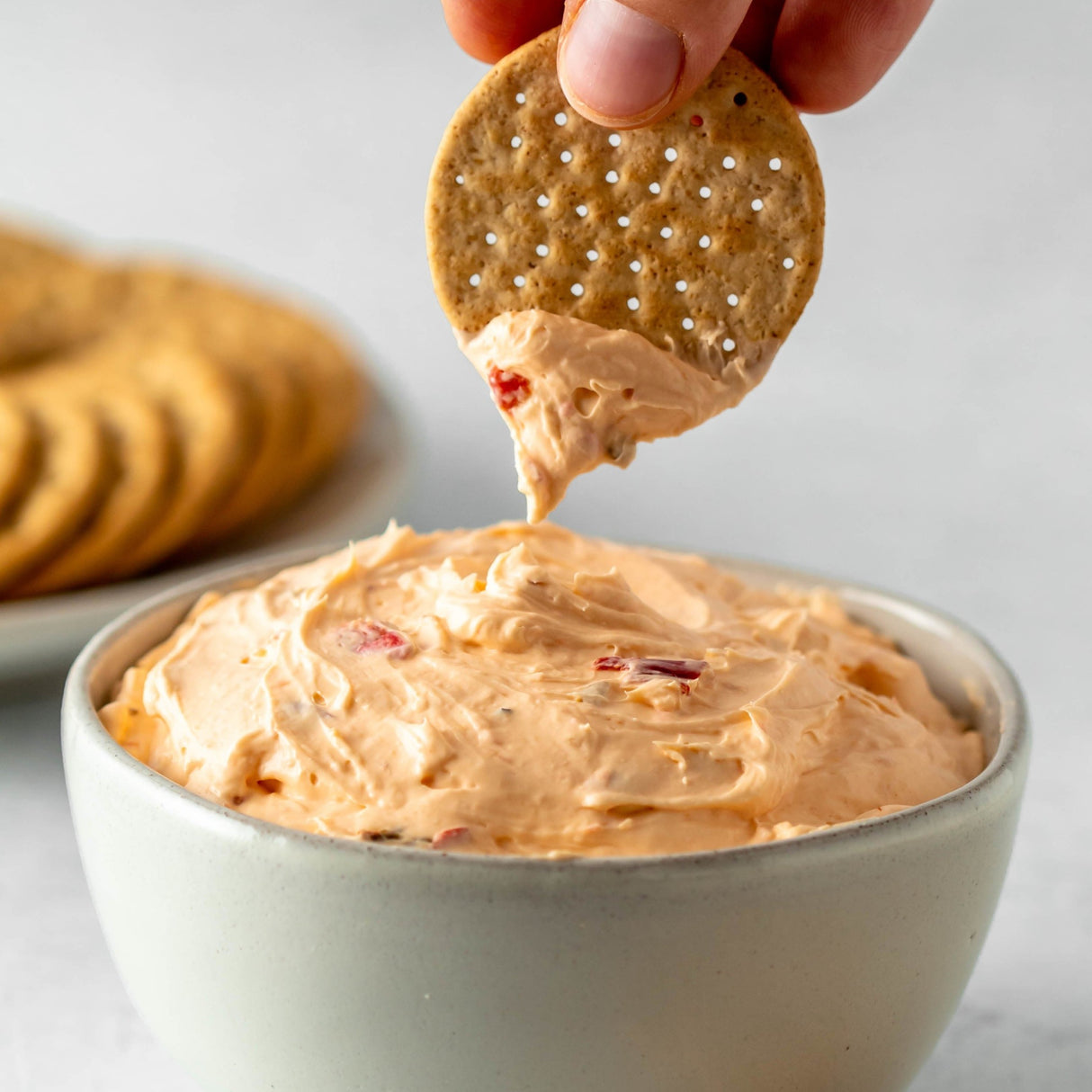 a cracker being dipped in cream cheese